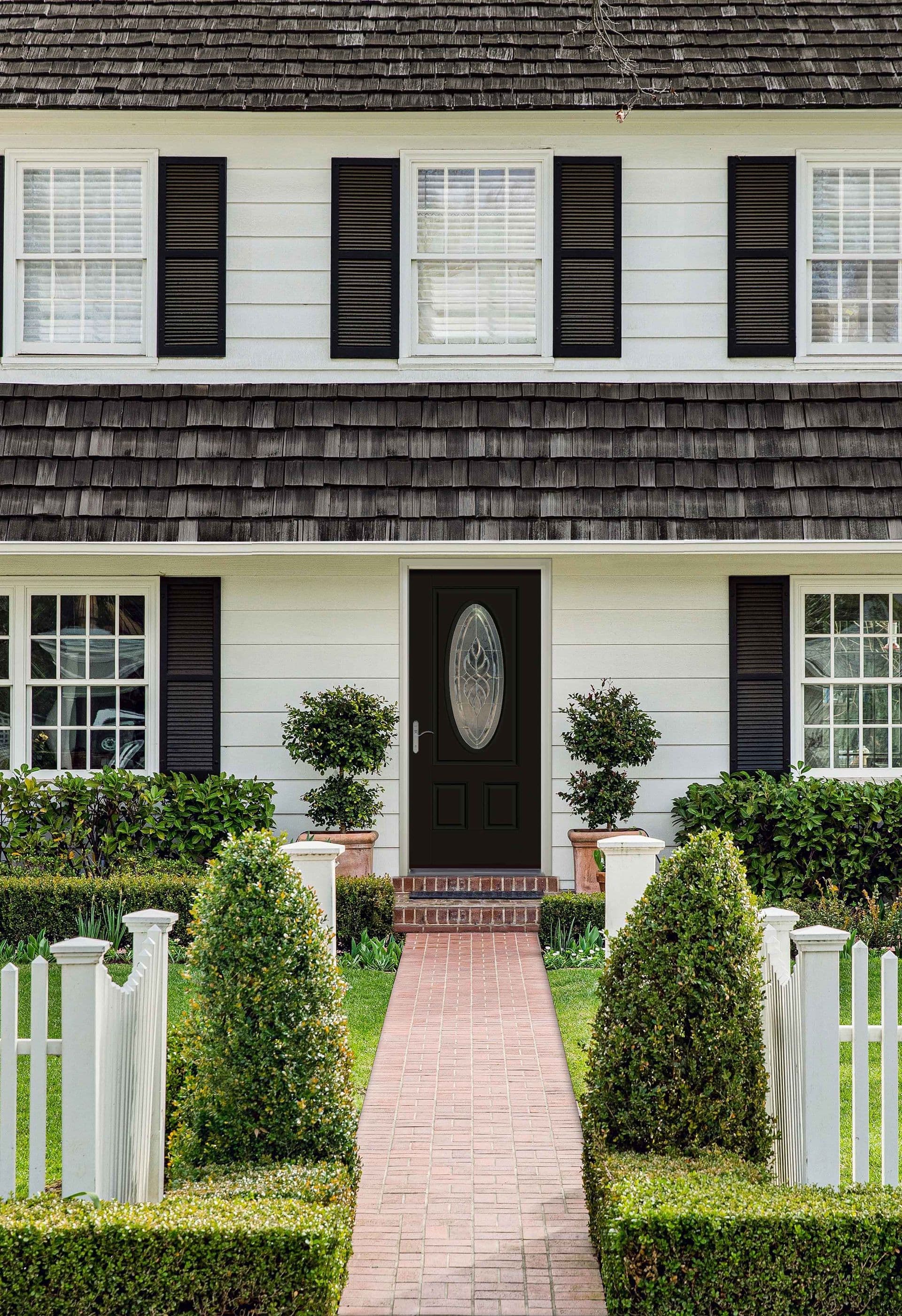 Two-story house with white siding and black shutters. A brick path leads to a black front door. Trimmed hedges and white picket fence enhance charm.