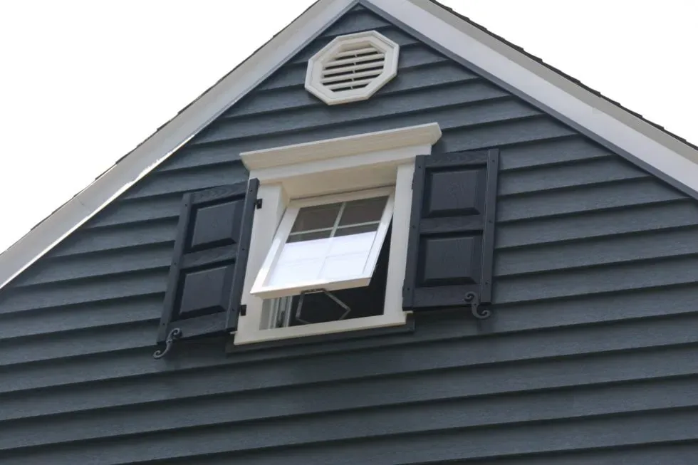 Gray house gable with a white window partially open. Decorative black shutters and an octagonal vent above convey a clean, modern style.