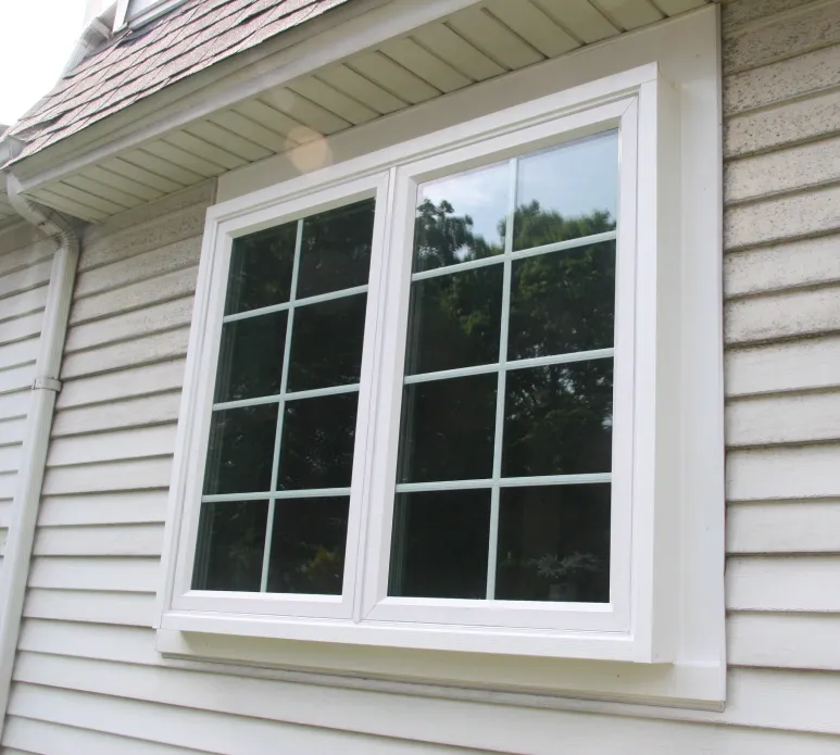 Double-hung window with white trim on a house exterior with gray siding. The window reflects trees, suggesting a sunny, peaceful atmosphere.